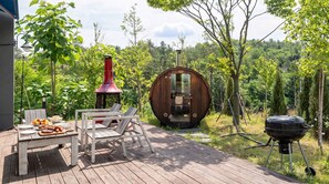 An outdoor deck with a barbecue grill, a wooden table with food, and a unique wooden structure. - Sokcho Biroso Private Cottage (Sokcho)
