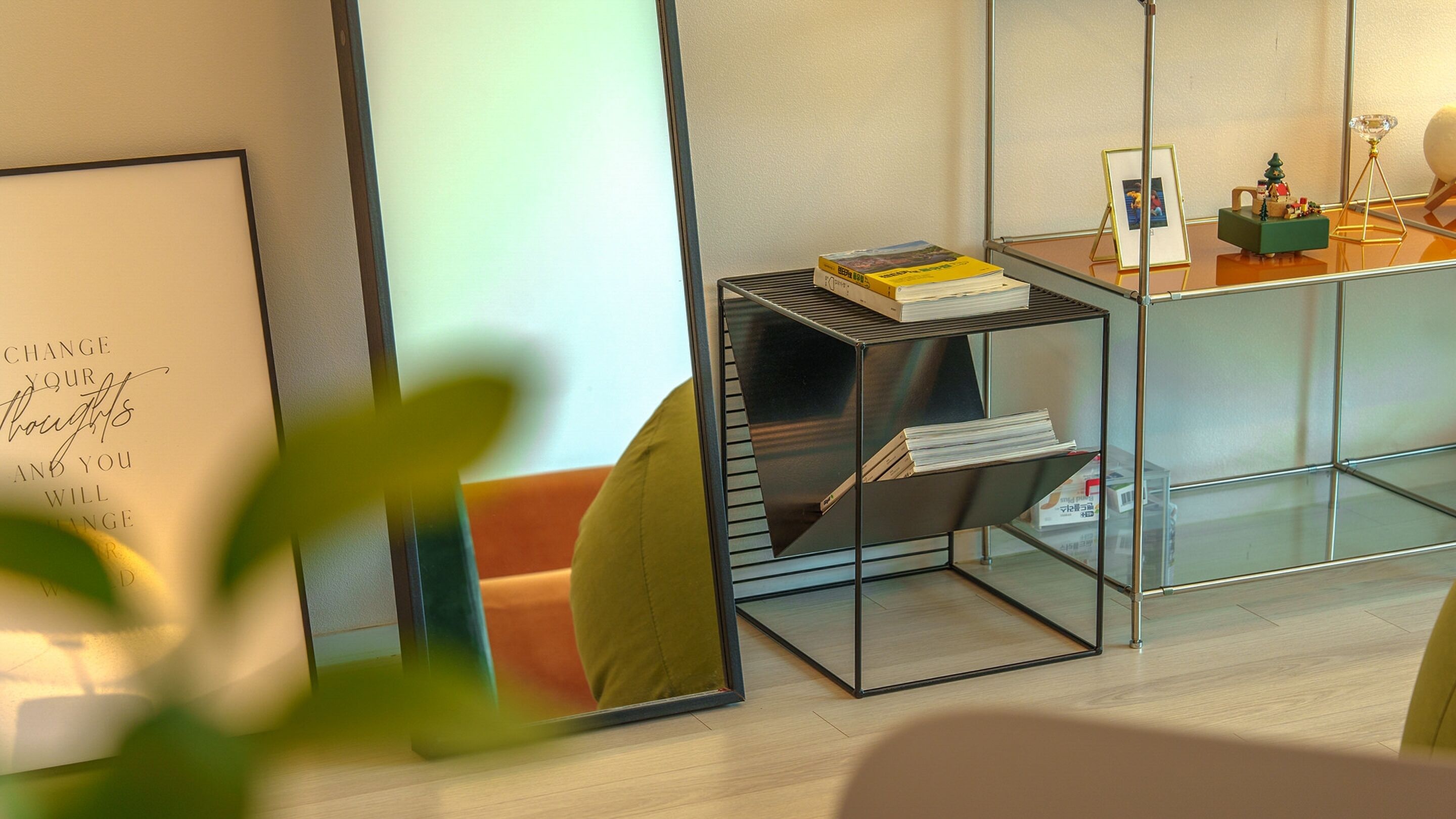 A modern room with a glass partition, a metal shelf with books, a framed inspirational quote, and a small Christmas tree decoration.