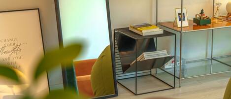 A modern room with a glass partition, a metal shelf with books, a framed inspirational quote, and a small Christmas tree decoration.