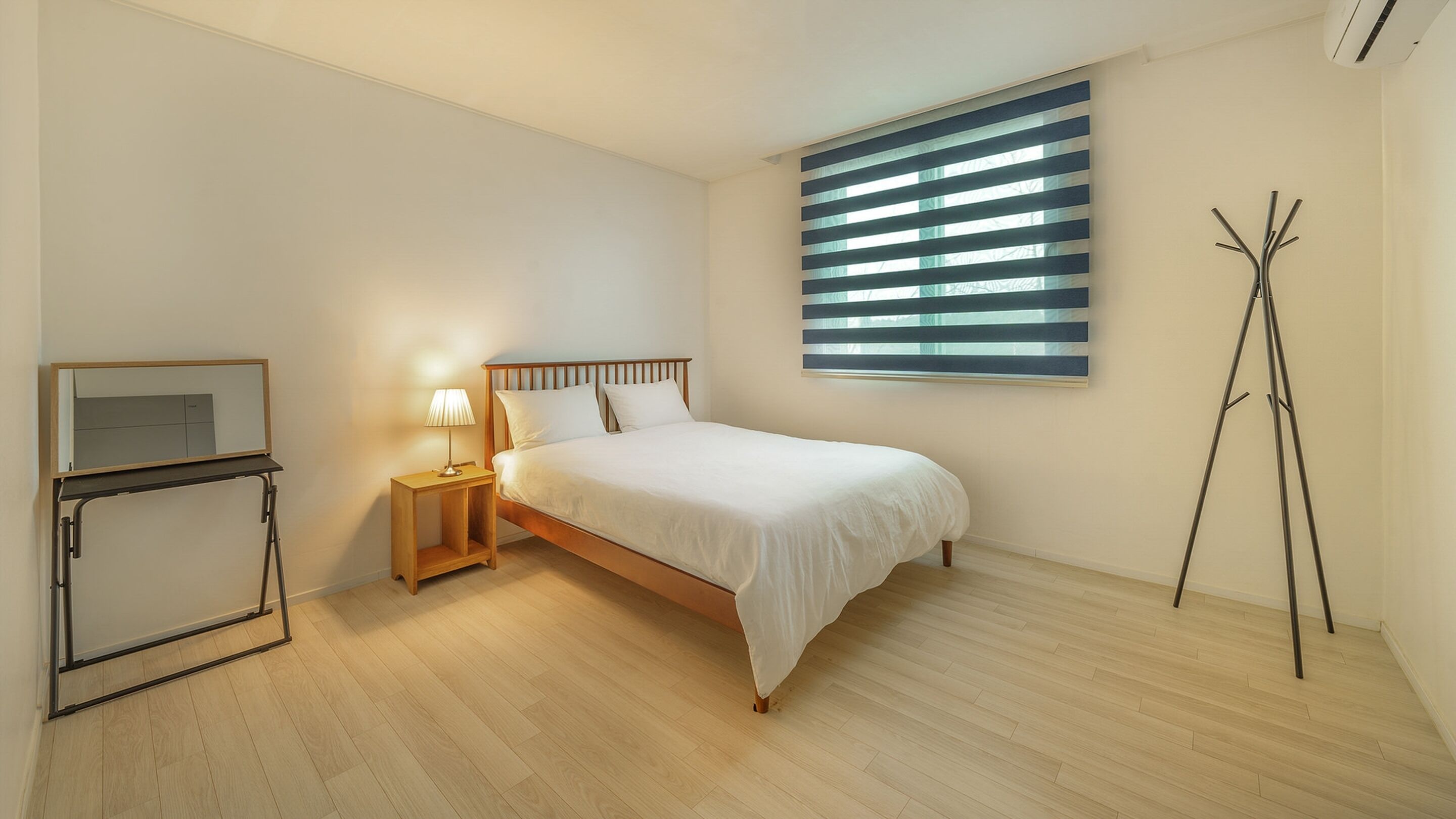 A bedroom with a bed, bedside table, lamp, and a tripod stand.