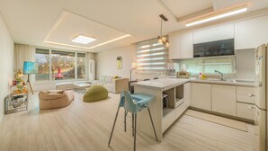 A modern kitchen with a central island, a dining area with a table and chairs, and a living area with a sofa and bean bag chairs. - Sokcho Biroso Private Cottage (Sokcho)