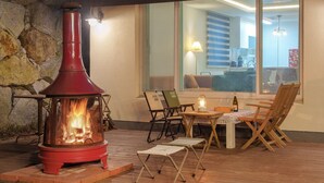 A cozy outdoor seating area with a wood-burning stove, a table with chairs, and a view of the interior through a large window. - Sokcho Biroso Private Cottage (Sokcho)