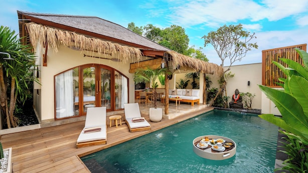 A poolside area with lounge chairs, a dining setup, and a thatched roof structure. - Villa Aldona by Pertama Stay (Tabanan)