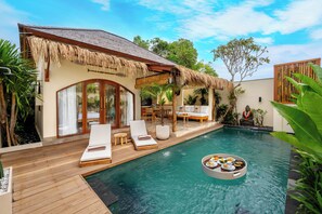Un espace aménagé au bord de la piscine, avec des chaises longues, un coin repas et une structure dotée d’un toit de chaume.