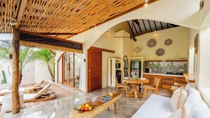A spacious living area with a wooden bench, a white sofa, and a dining table with chairs. - Villa Aldona by Pertama Stay (Tabanan)