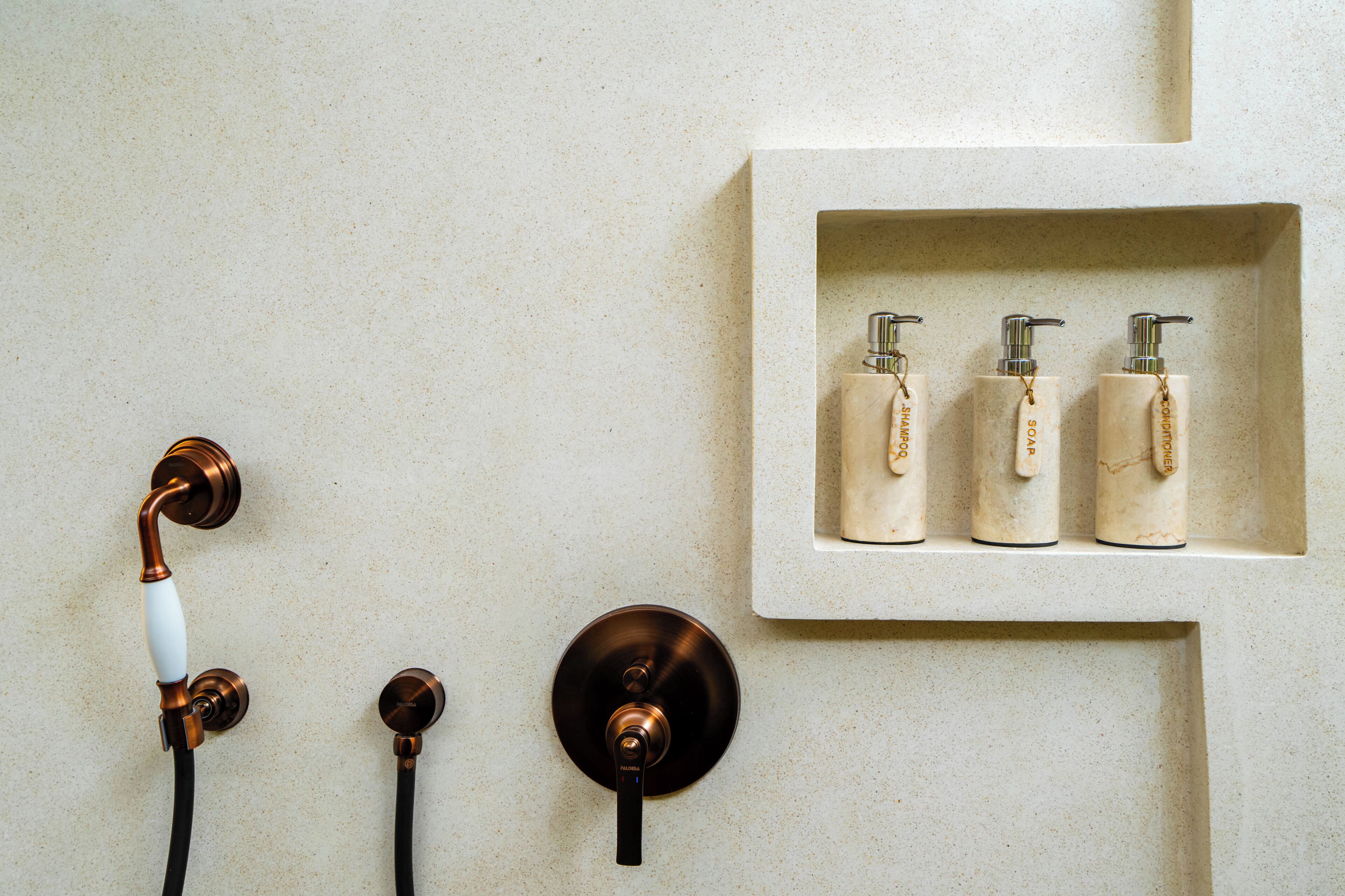 A bathroom with a shower, two faucets, and three bottles of shampoo and conditioner on a shelf.
