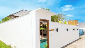 A modern white building with a pool, a wooden deck, and a clear blue sky. - Villa Aldona by Pertama Stay (Tabanan)