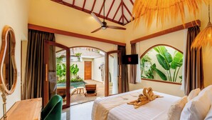 A hotel room with a bed, a desk, a chair, a TV, and a view of the outside. - Villa Aldona by Pertama Stay (Tabanan)