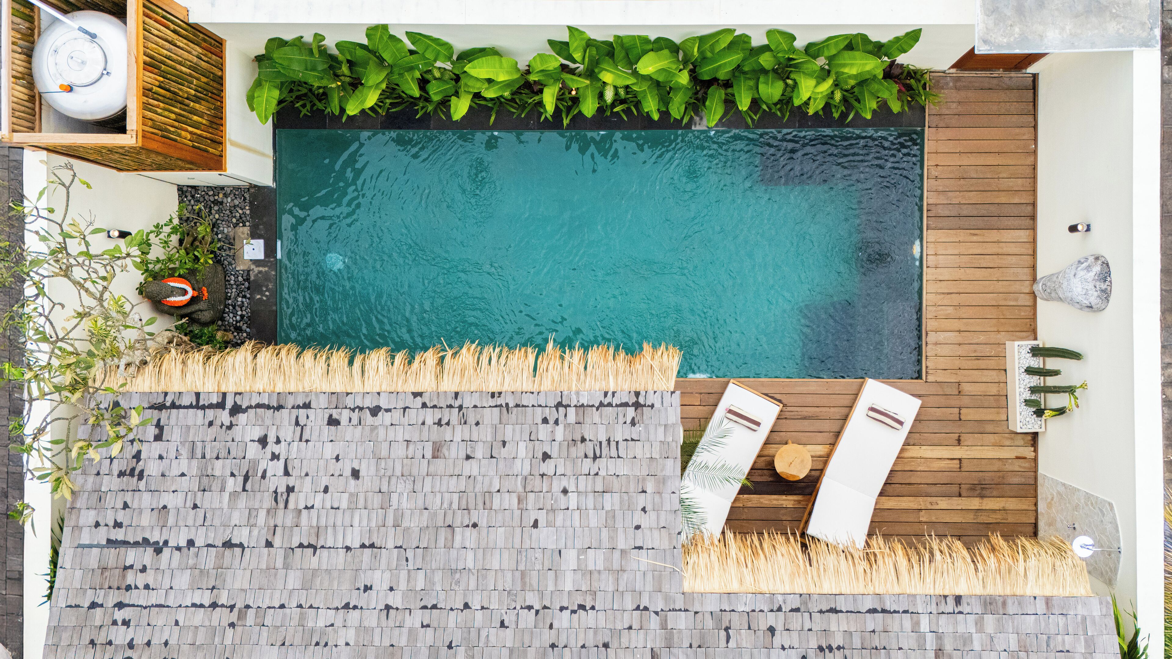 Una piscina en la azotea con terraza de madera, un pequeño jardín con plantas y un área de descanso con dos sillas y una mesa.