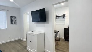 A spacious room with a large flat-screen TV mounted on the wall, a white cabinet, and a small desk with a chair.