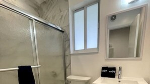 A bathroom with a glass-enclosed shower, a toilet, a sink, and a cabinet.