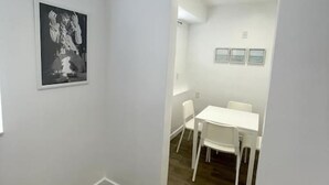 A room with a dining area featuring a white table and chairs, a framed picture on the wall, and a wooden floor.