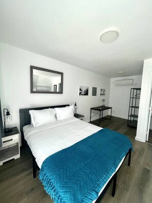 Un dormitorio moderno con una cama grande, una mesita de noche, un espejo y un pequeño escritorio con una silla.