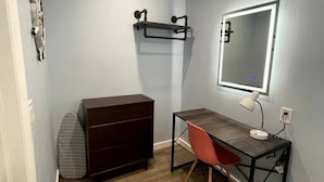 A small, well-lit room with a desk, chair, and dresser.