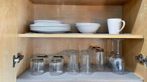 Ein Holzkabinent mit Regalen, auf denen Teller, Schüsseln, eine Tasse und Glasbehälter stehen.