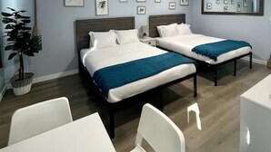 Une chambre d’hôtel avec deux lits, un bureau et une chaise. Les murs sont ornés de tableaux encadrés et il y a une plante en pot.