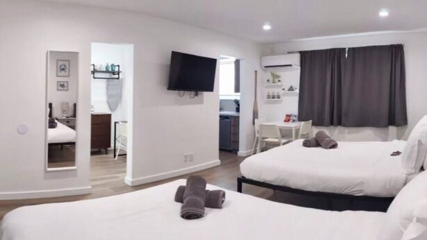 A hotel room with two beds, a TV mounted on the wall, a small kitchenette, and a separate dining area. - Charming DBL w/pool& parking 15 min to FLL & Beach (Hollywood)