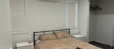 A bedroom with a bed, bedside tables, a wardrobe, and an air conditioning unit.