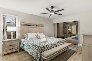 A bedroom with a bed, bedside table, lamp, bench, and a ceiling fan.