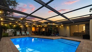A swimming pool with a covered patio area, outdoor seating, and string lights.