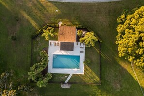An aerial view of a property with a swimming pool, surrounded by well-maintained lawns and trees.