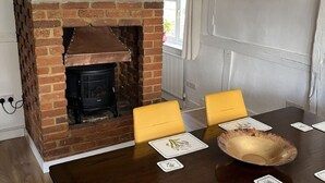 A dining area with a brick fireplace, yellow chairs, and a wooden table with placemats. - Home from home - classic country cottage with all amenities in peaceful village
 (Andover)
