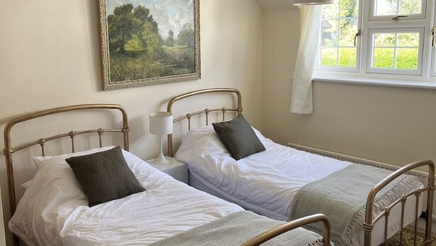 A room with two single beds, a painting on the wall, a window with curtains, and a hanging light fixture. - Home from home - classic country cottage with all amenities in peaceful village
 (Andover)