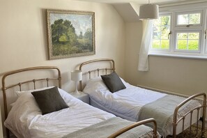 Ein Zimmer mit zwei Einzelbetten, einem Bild an der Wand, einem Fenster mit Vorhängen und einer Pendelleuchte.