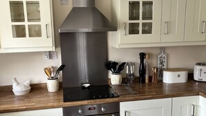A kitchen with white cabinets, a stainless steel range hood, a black induction cooktop, a white toaster, and a yellow towel hanging from the oven handle. - Home from home - classic country cottage with all amenities in peaceful village
 (Andover)