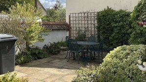 A patio with a table and chairs, surrounded by greenery and a white wall. - Home from home - classic country cottage with all amenities in peaceful village
 (Andover)