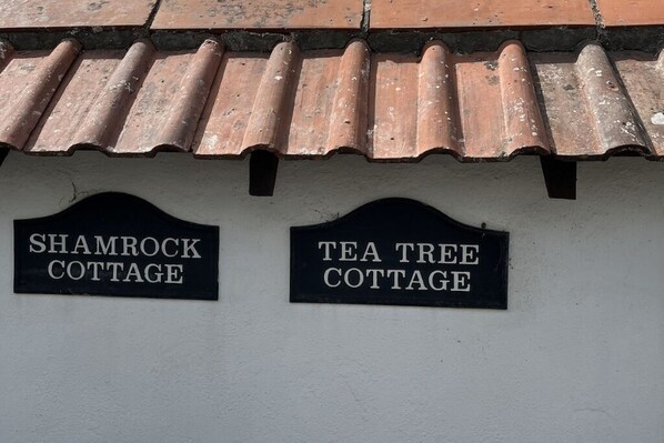 Zwei schwarze Schilder an einer Wand, eines mit der Aufschrift 'Shamrock Cottage' und das andere mit 'Tea Tree Cottage'.