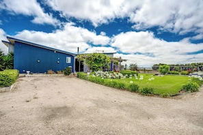 A blue building with a gravel driveway, a lawn with white flowers, and a clear sky.