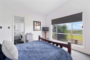 Quarto com uma janela grande, uma cama, uma cadeira, uma televisão e um quadro.