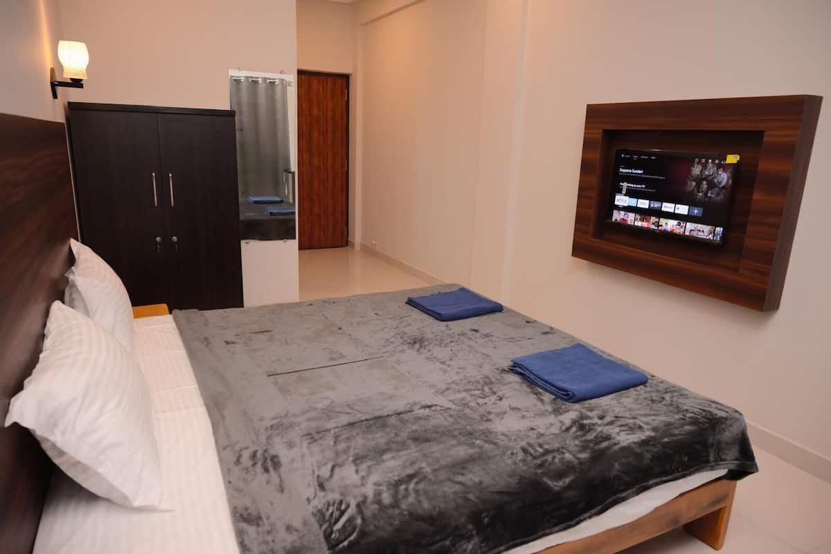 Une chambre à coucher comprenant un lit, une armoire, un téléviseur fixé au mur et une salle de bain visible à travers une porte.