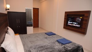 A bedroom with a bed, a wardrobe, a TV mounted on the wall, and a bathroom visible through a door. - Parth Guesthouse (Morjim)