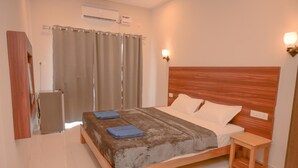 A bedroom with a wooden bed, a small bedside table, a wall-mounted air conditioner, and a curtain. - Parth Guesthouse (Morjim)