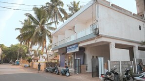 A building with a sign for M/S DELIGHT, a money exchange bureau. There are several parked scooters and a few people around. - Parth Guesthouse (Morjim)