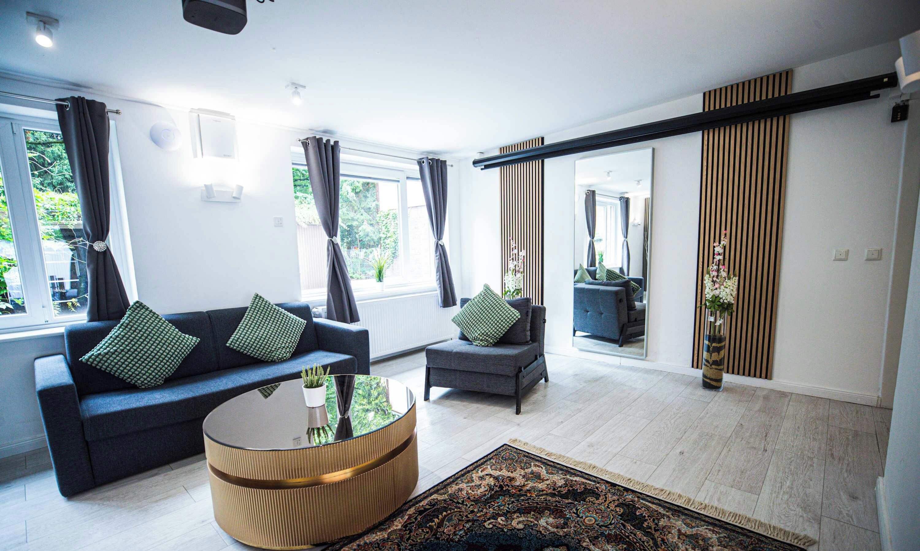 Una sala de estar moderna con sofá, sillón y mesa de centro, un espejo grande y vistas al exterior.