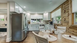 Une cuisine moderne avec des meubles blancs, un réfrigérateur en acier inoxydable et un coin repas en bois avec une table ronde.