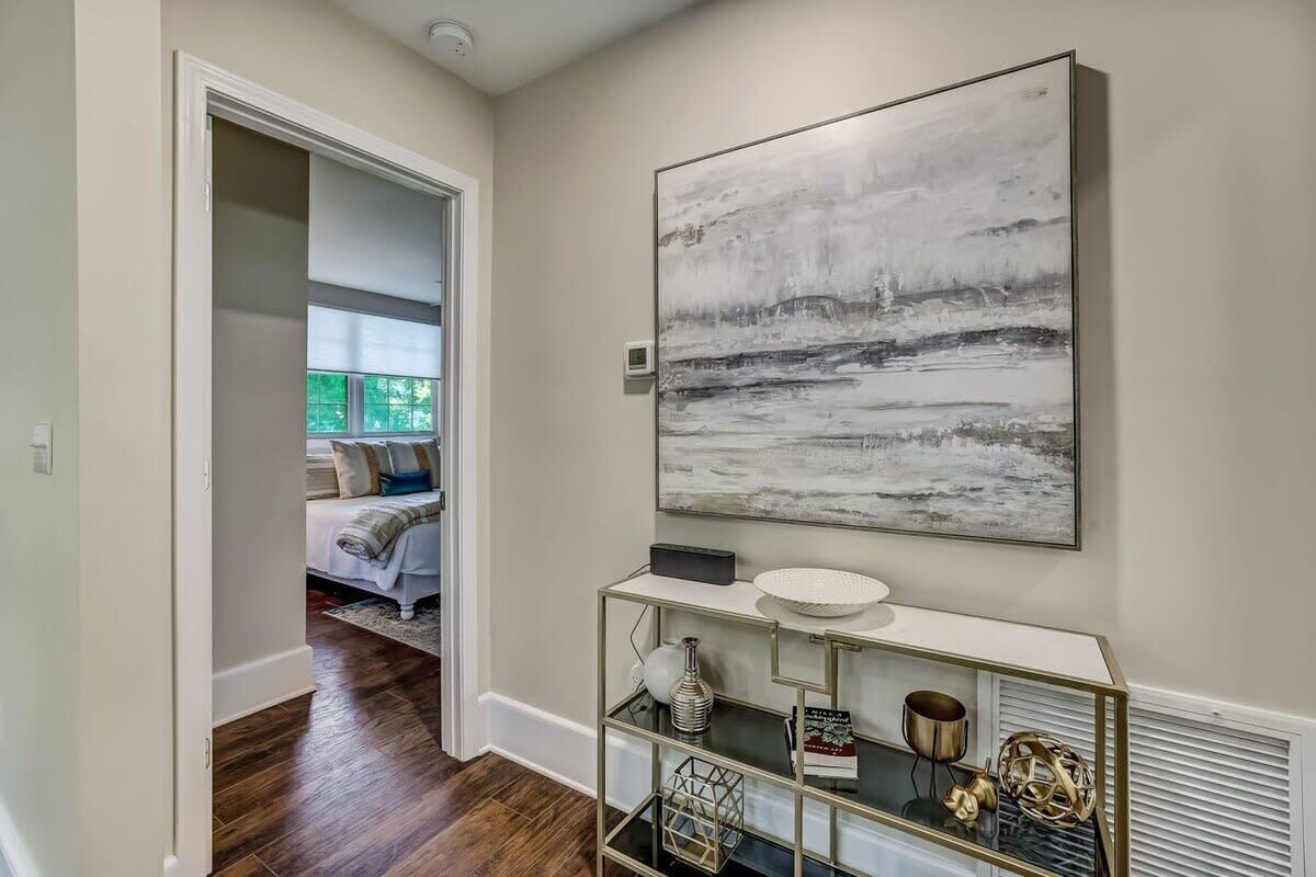 A hallway with a modern console table, a large abstract painting, and a glimpse of a bedroom with a bed and window.