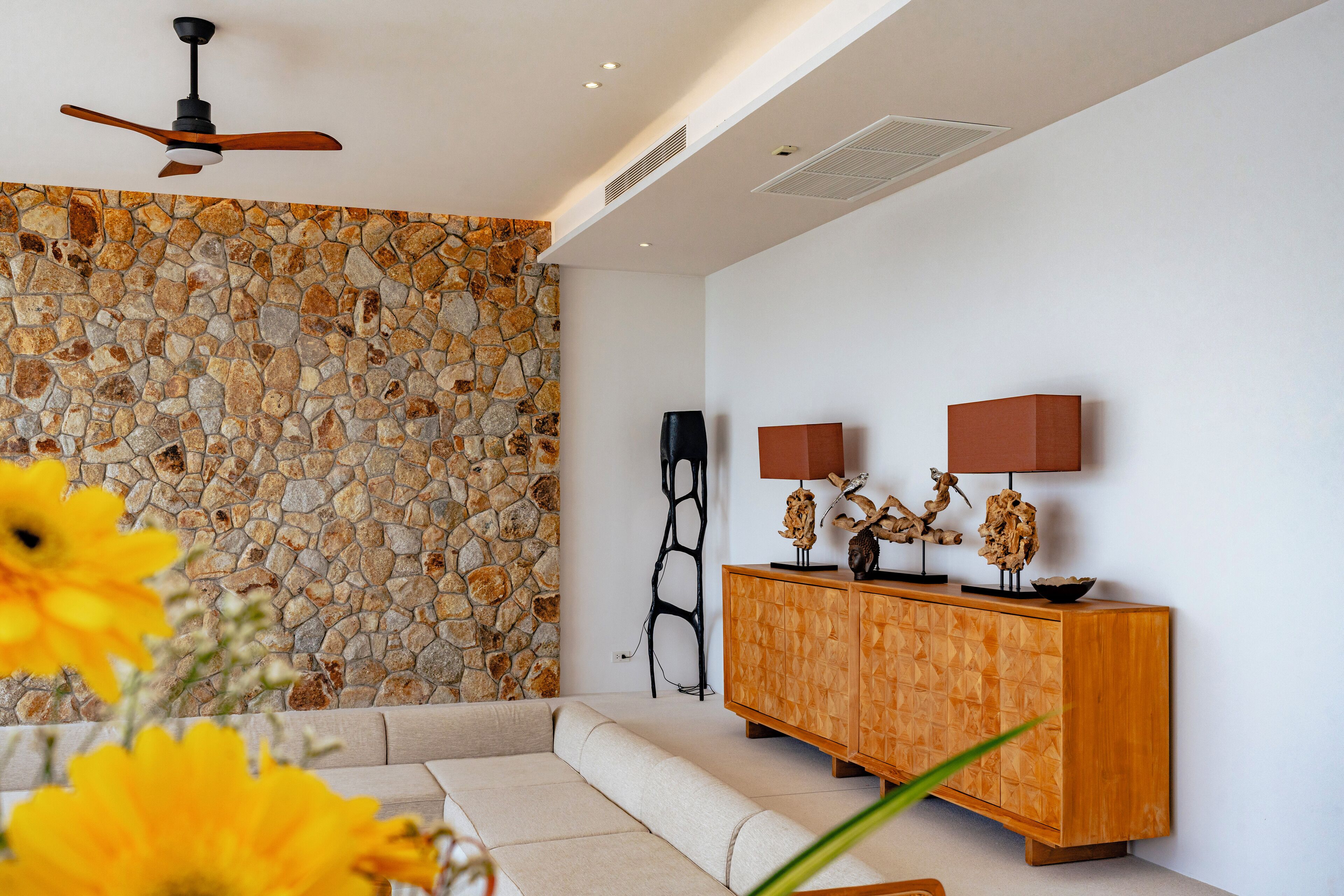 Un salon moderne avec un mur en pierre, un meuble en bois agrémenté d’objets décoratifs et un ventilateur de plafond.