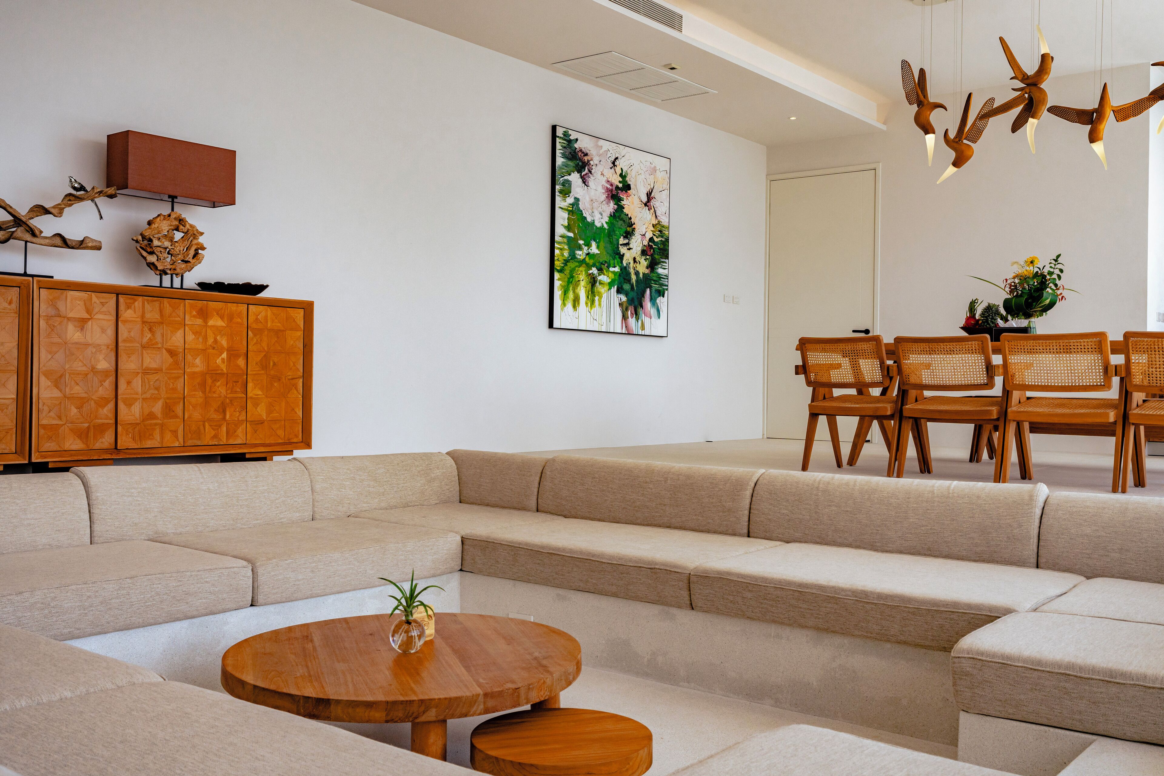 Una sala de estar moderna con un sofá modular, una mesa de centro de madera y un comedor con sillas de mimbre.