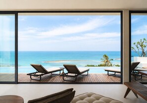 A room with a large window overlooking a beach and ocean. There are three lounge chairs and a small table. - Anzhu Seamate Villa Samui (Koh Samui)