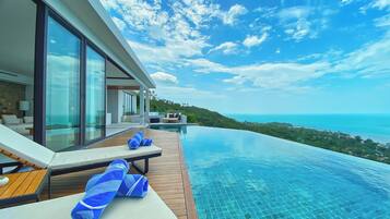 A modern infinity pool with a clear view of the ocean and a lush green landscape.