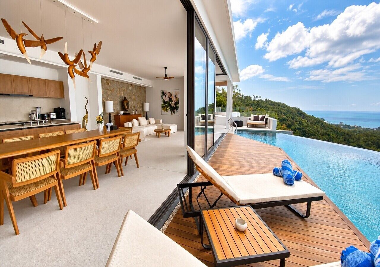 Uma cozinha moderna com armários de madeira, uma área de refeições com cadeiras de vime, um espaço de descanso à beira da piscina com vista para o oceano e uma grande janela com vista para a paisagem.