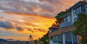 A modern two-story building with a stone facade and large windows, surrounded by lush greenery and palm trees, overlooking a scenic landscape. - Anzhu Seamate Villa Samui (Koh Samui)