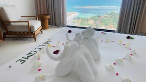 Ein Zimmer mit großem Fenster, einem Bett mit Handtüchern und Blumen sowie einem Sessel.