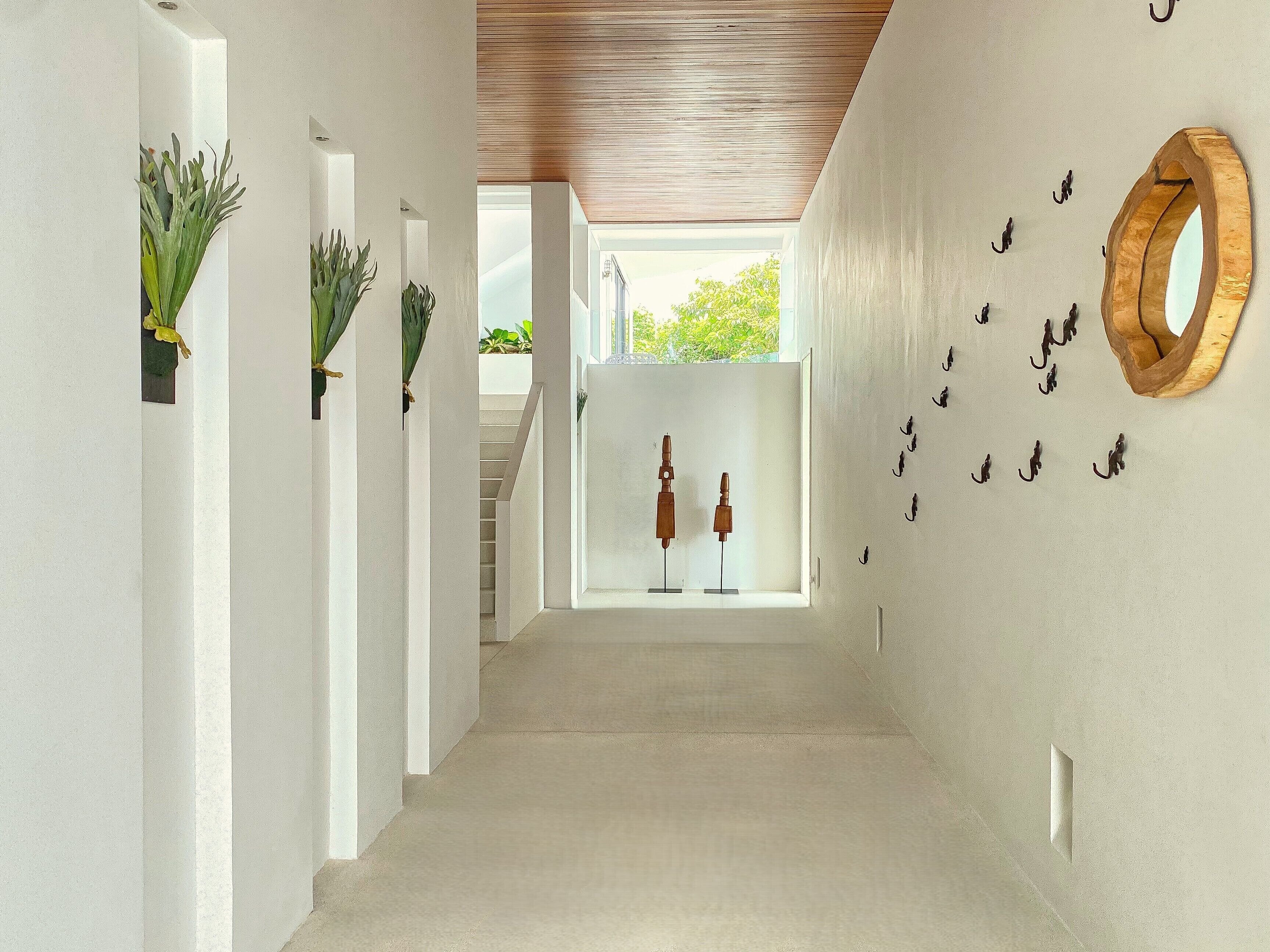 A hallway with white walls, a wooden ceiling, and a view of a staircase leading to a balcony.