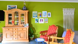 Ein Wohnzimmer mit grüner Wand, Holzmöbeln und verschiedenen gerahmten Kunstwerken.