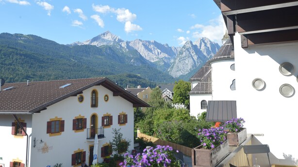 Blick auf Berge mit einem Gebäude, das einen Balkon und ein Schild mit der Aufschrift "MUMBAHLÄTZ" hat.